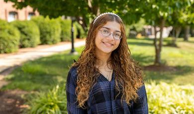 Portrait photo of Sofie De Coste standing in front of trees and grass on a sunny day.